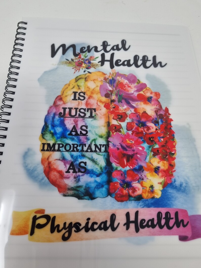 K&ouml;nnte beinhalten: Ein farbenfrohes Notizbuch mit Spiralbindung. Der Einband zeigt eine Aquarell-Illustration eines Gehirns mit Blumen und dem Text "Mentale Gesundheit ist genauso wichtig wie k&ouml;rperliche Gesundheit."