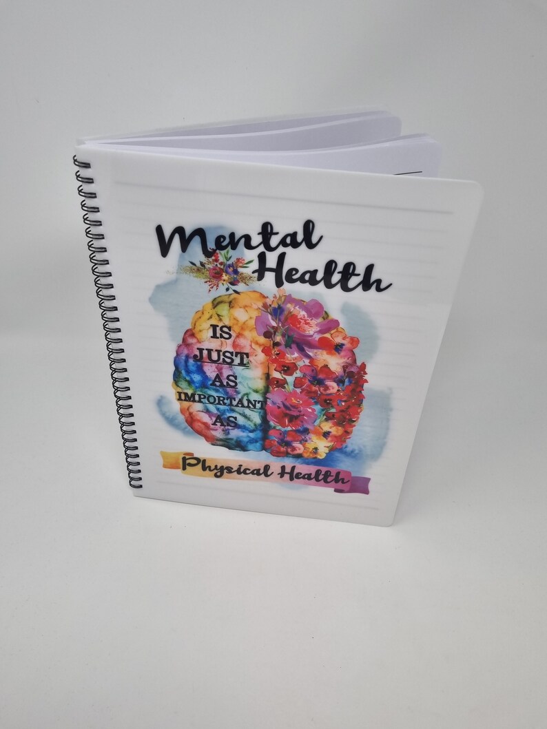 K&ouml;nnte beinhalten: Ein wei&szlig;es Spiralnotizbuch mit dem Text "Mental Health is just as important as Physical Health" auf dem Cover. Der Text ist schwarz und das Cover zeigt eine farbenfrohe Aquarellillustration eines Gehirns mit Blumen.
