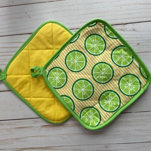 May include: Two yellow quilted pot holders with green trim. One pot holder has a lime pattern on a yellow background with white stripes.
