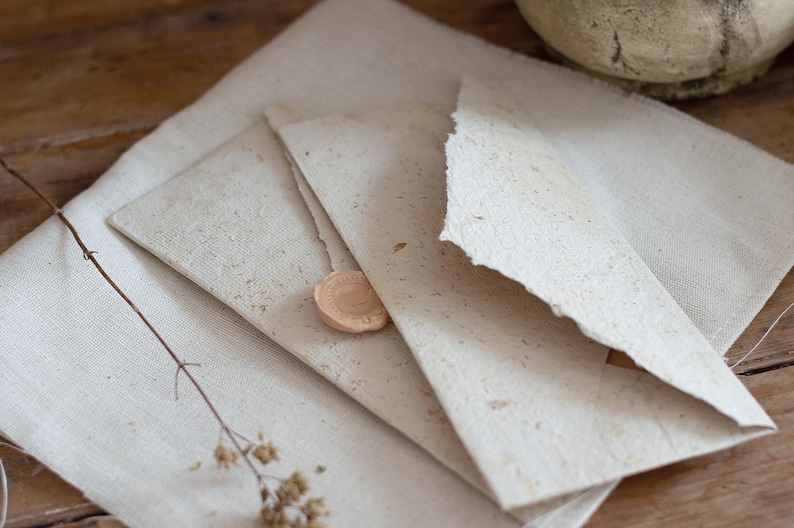 May include: A set of three off-white envelopes with a textured surface and a wax seal. The envelopes are stacked on top of each other.