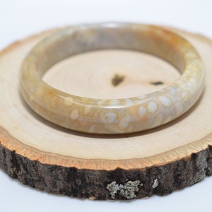 May include: A white and beige fossilized coral bangle bracelet. The bracelet is smooth and polished, with a natural, organic look.