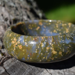 May include: A green, blue, and gold speckled stone bangle bracelet. The bracelet is smooth and polished.