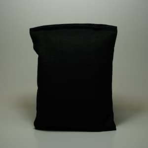 May include: A black fabric pouch with a smooth, flat surface. The pouch is folded and sitting on a white surface.