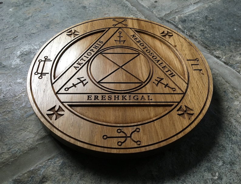 Op de afbeelding: Een houten cirkel met een gesneden ontwerp met een driehoek met de woorden "Aktophis", "Ereshkigal" en "Nebotoscoalethe" eromheen gegraveerd.