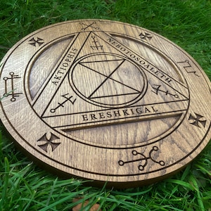 Op de afbeelding: Een houten cirkel met een driehoekig ontwerp en de woorden "AKTIOPHIS", "NEBOTOSOALETH" en "ERESH KIGAL" die rond de omtrek zijn gegraveerd.