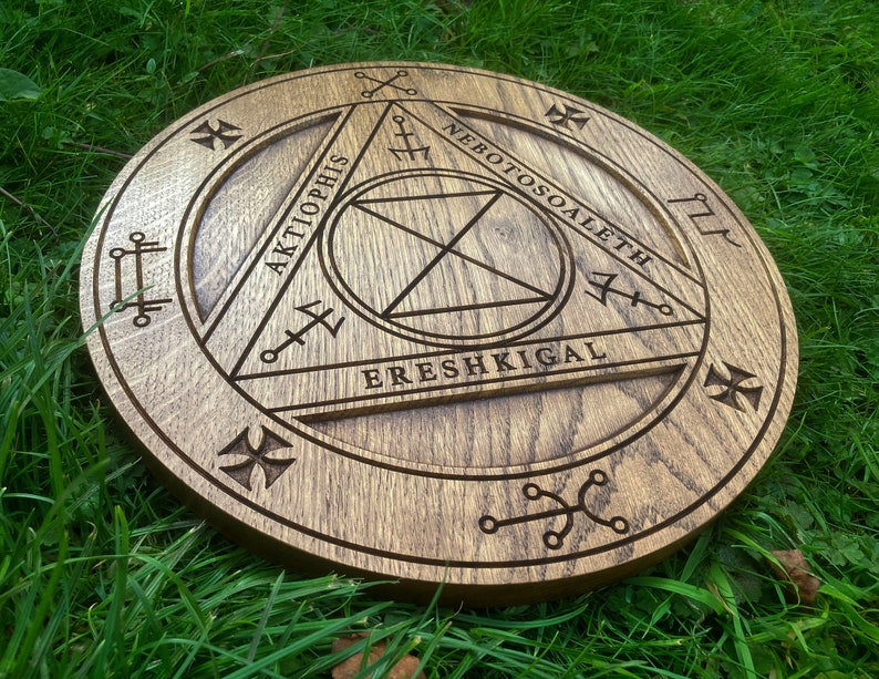 Op de afbeelding: Een houten cirkel met een driehoekig ontwerp en de woorden "AKTIOPHIS", "NEBOTOSOALETH" en "ERESH KIGAL" die rond de omtrek zijn gegraveerd.