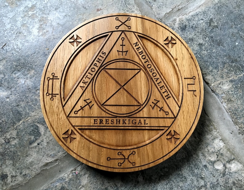 Op de afbeelding: Een houten cirkel met een geometrisch ontwerp en de woorden "Aktiophis", "EreShkigal" en "Nebotosoaleth" die rond de omtrek zijn gegraveerd.