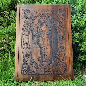 May include: A wooden plaque with a carved image of a winged figure surrounded by a circle of zodiac signs. The figure is holding a staff and has a crown on its head. The plaque is dark brown and has a natural wood grain.