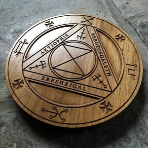 Op de afbeelding: Een houten cirkel met een gesneden ontwerp met de woorden "Aktiophis", "Ereshkigal" en "Nebotososaleth".