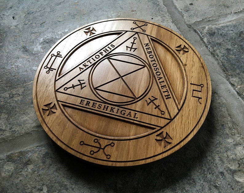 Op de afbeelding: Een houten cirkel met een gesneden ontwerp met de woorden "Aktiophis", "Ereshkigal" en "Nebotososaleth".