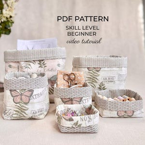 Op de afbeelding: Een set van vijf stoffen opbergmanden in verschillende maten met een vintage print van vlinders, varens en postzegels. Elke mand heeft een bovenrand met een geweven uiterlijk. Tekst: PDF PATTERN, SKILL LEVEL BEGINNER, video tutorial.
