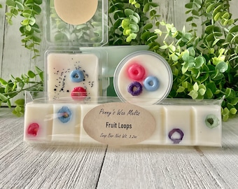 Puede incluir: Una barra de cera para derretir blanca con una etiqueta que dice "Penny's Wax Melts Fruit Loops Snap Bar Net Wt. 3.2oz". La barra está dividida en seis cuadrados, cada uno con un diseño diferente de bucles de frutas de colores.