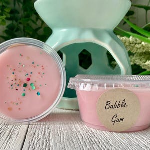 May include: Two small containers of pink wax melt with glitter. One container has a label that says "Bubble Gum".