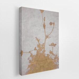 May include: A canvas print featuring a botanical design. The artwork showcases a gold-colored floral silhouette against a textured, light gray background. The flowers and stems are detailed, creating a natural and elegant aesthetic. The canvas is mounted on a wooden frame.