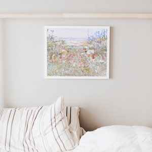 K&ouml;nnte beinhalten: Ein gerahmter Druck eines bunten Wildblumenfeldes in einem wei&szlig;en Rahmen. Das Kunstwerk zeigt eine Vielzahl von Blumen in Rot-, Blau-, Gelb- und Wei&szlig;t&ouml;nen. Der Druck h&auml;ngt an einer hellgrauen Wand &uuml;ber einem Bett mit gestreiften Kissen und einer wei&szlig;en Bettdecke.