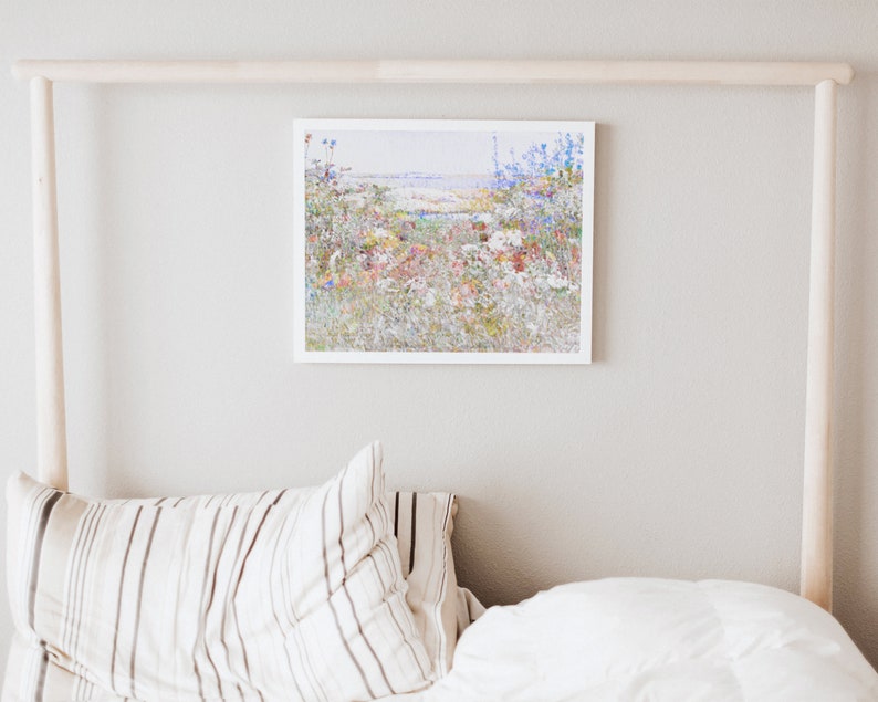 K&ouml;nnte beinhalten: Ein gerahmter Druck eines bunten Wildblumenfeldes in einem wei&szlig;en Rahmen. Das Kunstwerk zeigt eine Vielzahl von Blumen in Rot-, Blau-, Gelb- und Wei&szlig;t&ouml;nen. Der Druck h&auml;ngt an einer hellgrauen Wand &uuml;ber einem Bett mit gestreiften Kissen und einer wei&szlig;en Bettdecke.