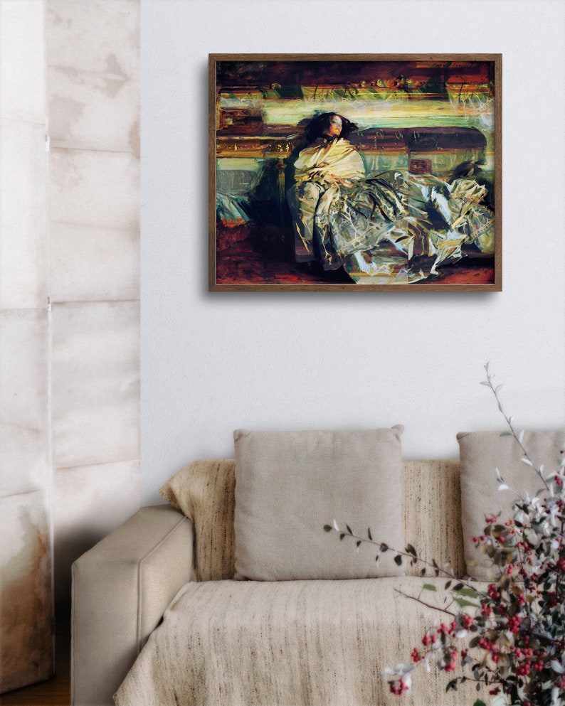 May include: A framed artwork depicts a person draped in a yellow shawl, seated on a couch. The painting features a palette of muted greens, browns, and yellows, with visible brushstrokes. The artwork is displayed above a beige couch with matching pillows.
