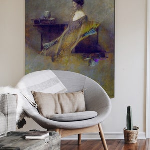 May include: An antique-style painting of a woman in a flowing gown, with a neutral colour palette. The artwork hangs above a modern grey chair with a tan cushion and a striped blanket. A wooden coffee table and a small cactus in a woven pot complete the scene.