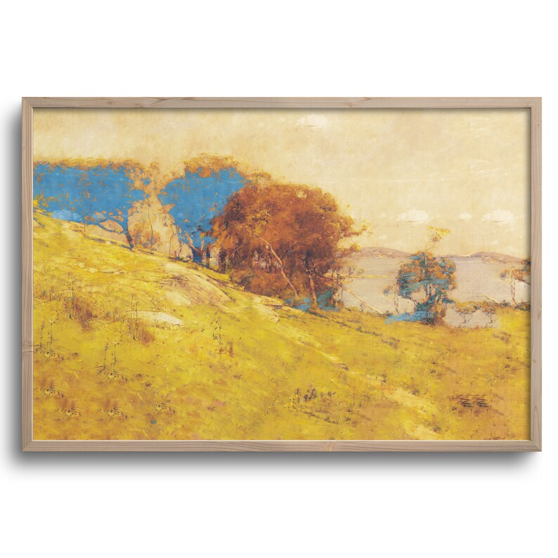 May include: A framed landscape painting featuring a hillside with yellow grass and trees with blue and brown foliage. A body of water is visible in the background under a light yellow sky. The artwork is in a light wood frame.