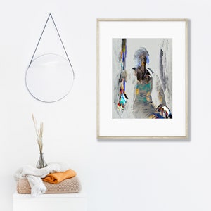 May include: Abstract art print in a light wood frame. The artwork features a seated figure with colorful brushstrokes. A round mirror hangs on the wall, and a stack of folded blankets and a vase with dried plants are on a white cabinet.