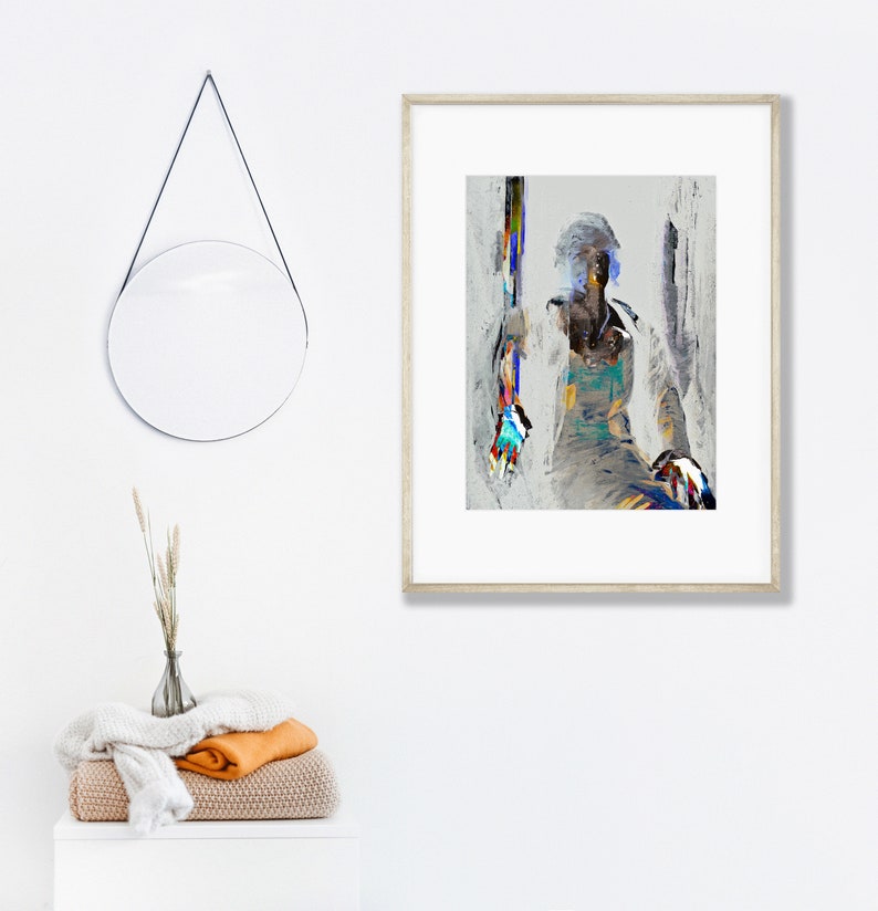 May include: Abstract art print in a light wood frame. The artwork features a seated figure with colorful brushstrokes. A round mirror hangs on the wall, and a stack of folded blankets and a vase with dried plants are on a white cabinet.