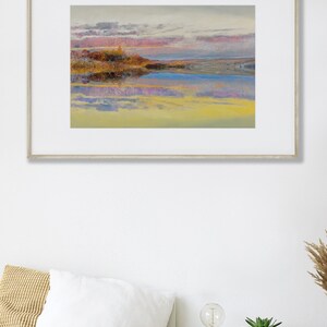 May include: A framed landscape painting with a serene waterscape. The artwork features a colorful sky with pink and gray clouds reflected in the water. The painting is displayed above a bed with white linens.