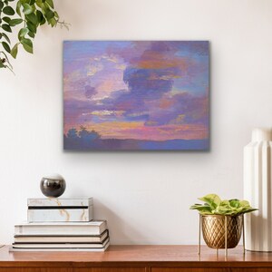 May include: A square canvas art piece depicting a sunset with a dramatic cloudscape. The sky transitions from pink and gold to shades of purple and blue. The artwork is displayed above a wooden dresser with decorative items.