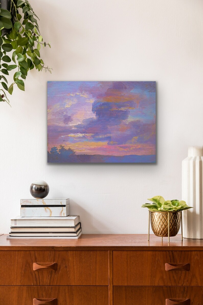 May include: A square canvas art piece depicting a sunset with a dramatic cloudscape. The sky transitions from pink and gold to shades of purple and blue. The artwork is displayed above a wooden dresser with decorative items.