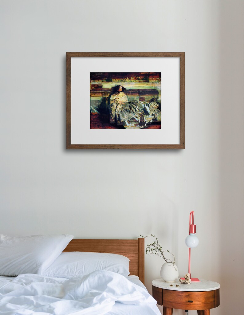 May include: A framed artwork depicting a woman in a flowing gown, resting on a sofa. The painting features a palette of muted greens, reds, and golds, with a focus on the textures of the fabric and the figure's pose. The frame is a warm brown.