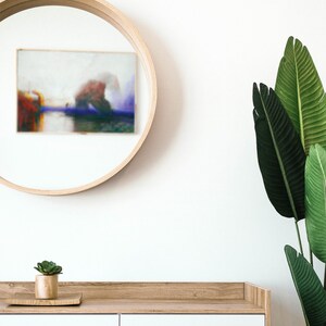 May include: A contemporary interior scene with a circular wooden mirror displaying a blurred painting, a white cabinet with wooden detailing, a small succulent plant, and large green leaves. The design creates a minimalist and natural aesthetic.