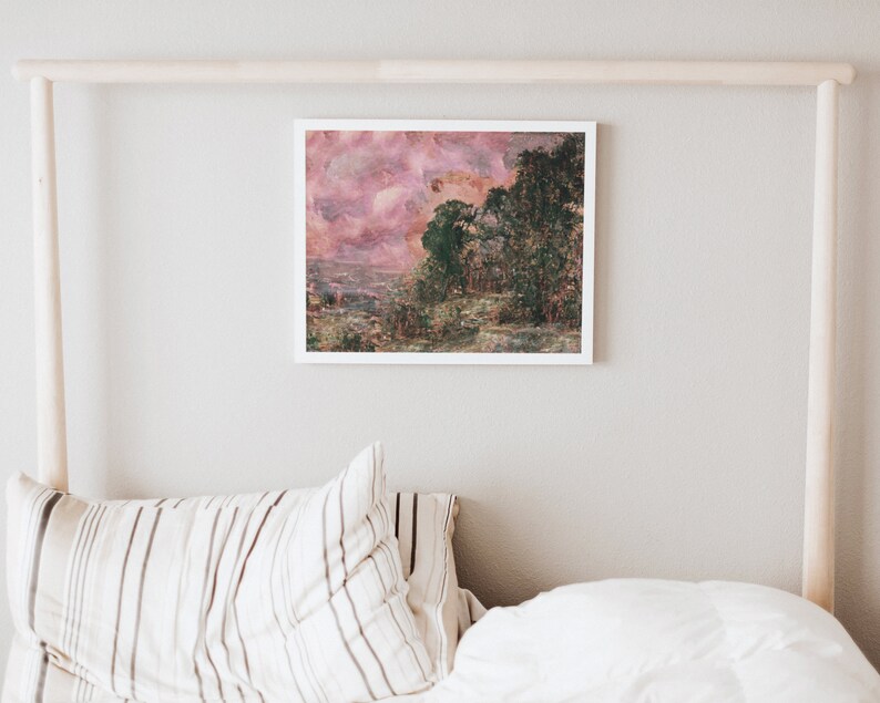 May include: A framed landscape art print featuring a pink and green color palette. The artwork depicts a forest scene with a cloudy sky. The print is displayed on a white wall above a bed with striped pillows and a white comforter.