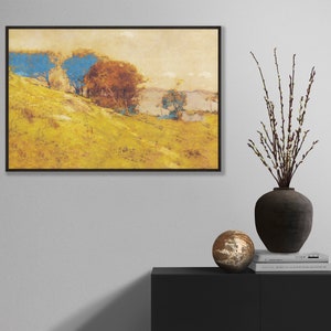 May include: An art print in a black frame depicts a landscape with a yellow hillside, blue and brown trees, and a body of water in the background. A dark vase with branches and a decorative sphere sit on a black cabinet.
