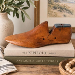 May include: A vintage wooden shoe last with a natural brown finish and a blue painted heel section. The object features a segmented design with visible metal hardware joints and small circular holes along the side of the wooden form.
