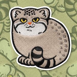 Puede incluir: Parche bordado de un gato gris y blanco con rayas negras. El gato tiene ojos amarillos y una expresión seria.