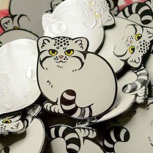 Könnte beinhalten: Eine Sammlung von weißen und schwarzen Emaille-Pins mit verschiedenen niedlichen Comic-Katzen mit unterschiedlichen Gesichtsausdrücken. Die Pins sind alle in verschiedenen Größen und Formen, und einige haben Streifen oder Flecken.