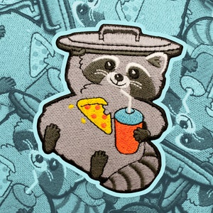 May include: Embroidered patch of a grey raccoon wearing a bin lid as a hat, holding a pizza slice and a red cup with a straw. The raccoon has a black nose and eyes, and a white stripe on its forehead.