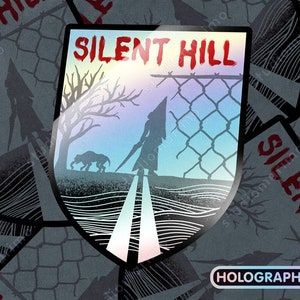 May include: A holographic sticker featuring the words "SILENT HILL" in red text. The sticker is shaped like a shield and features a silhouette of a figure with a pyramid head walking down a road with a fence in the background. The sticker has a holographic finish.