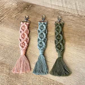 May include: Three macrame keychains with tassels. The keychains are pink, light blue, and green.