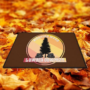 May include: A brown doormat with a circular logo featuring a pine tree and the text "Morning Wood Lumber Company". The logo has a pink, orange, and yellow gradient.