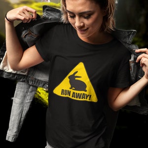 Peut inclure: Un t-shirt noir avec un panneau d'avertissement jaune représentant une silhouette de lapin et le texte "RUN AWAY!"