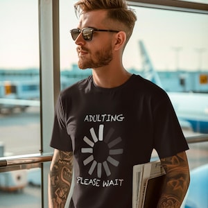 May include: A black t-shirt with a white graphic of a loading circle and the text "Adulting Please Wait".