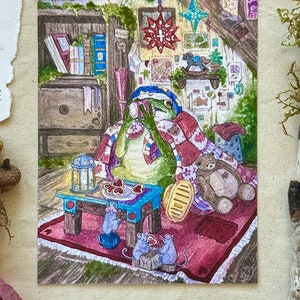 Peut inclure: Illustration à l'aquarelle d'une grenouille dans un cadre douillet, buvant dans une tasse. La grenouille est enveloppée dans une couverture, entourée de livres, d'un cheval à bascule et d'un ours en peluche. Une petite table présente des biscuits en forme de cœur et une lanterne.