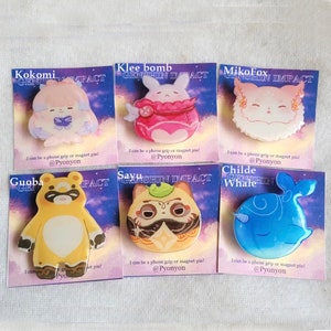 May include: Six colorful enamel pins featuring characters from the video game Genshin Impact. The pins are on white card stock with the character's name and the game's title. The pins can be used as phone grips or magnet pins.