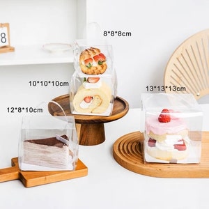 May include: Four clear plastic boxes with lids and handles, containing different types of cakes and pastries. The boxes are labeled with their dimensions in inches: 8x8x8, 10x10x10, 12x8x10, and 13x13x13.