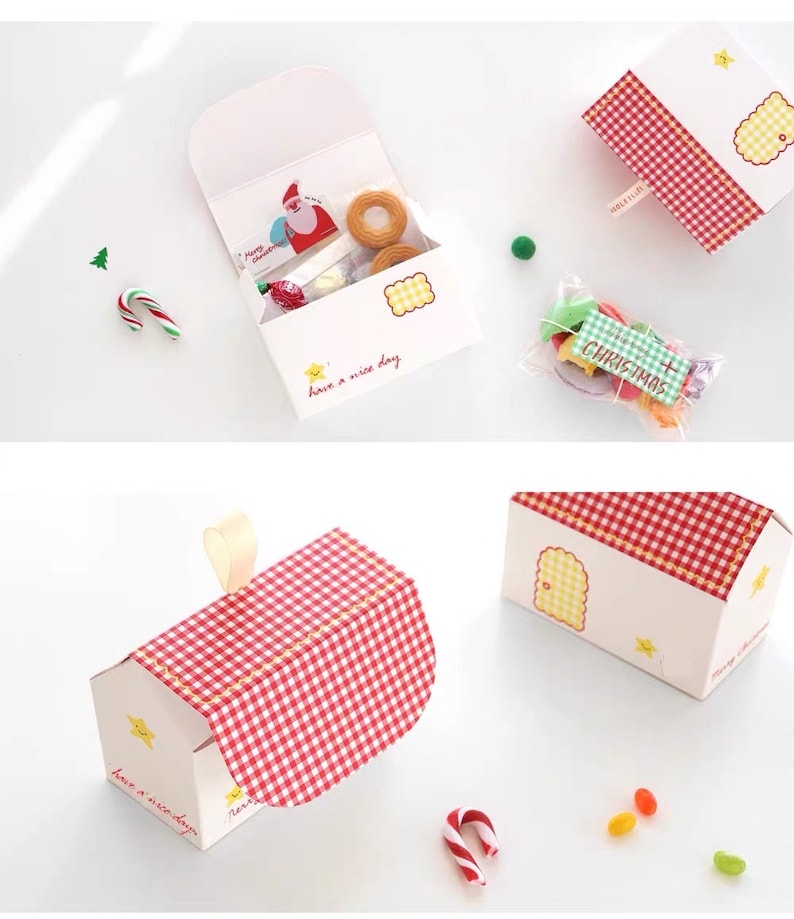 May include: A set of three red and white gingham patterned gift boxes with a white background. The boxes are shaped like houses with a star and the text "have a nice day" on the front. The boxes are filled with small candies and treats.