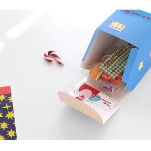 May include: A blue and white gift box with a checkered pattern and the text "Love & Sweet Life" on the side. The box is open and contains a variety of colorful candies and a small card with the text "Merry Christmas!"