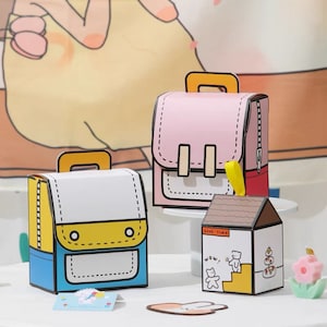 May include: Three colorful papercraft boxes shaped like backpacks and a house. The backpacks have yellow, blue, and pink accents. The house has a brown roof and white walls with the text "Good Time" and a cartoon bear.