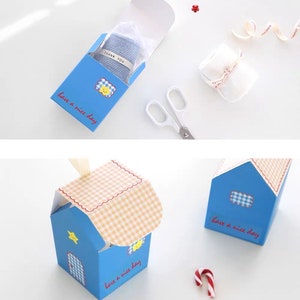 May include: A blue and white gift box with a checkered pattern on the lid. The box has a house shape and says "have a nice day" on the front. The box is open and a small blue and white striped item is inside.
