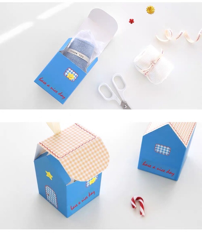 May include: A blue and white gift box with a checkered pattern on the lid. The box has a house shape and says "have a nice day" on the front. The box is open and a small blue and white striped item is inside.