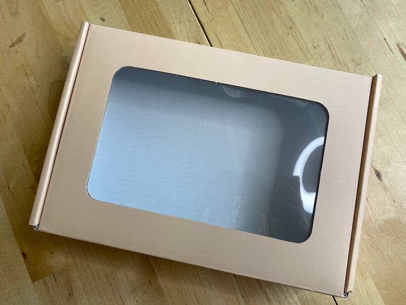 Puede incluir: Una caja de cart&oacute;n marr&oacute;n claro con una ventana transparente en la parte delantera. La caja est&aacute; vac&iacute;a.